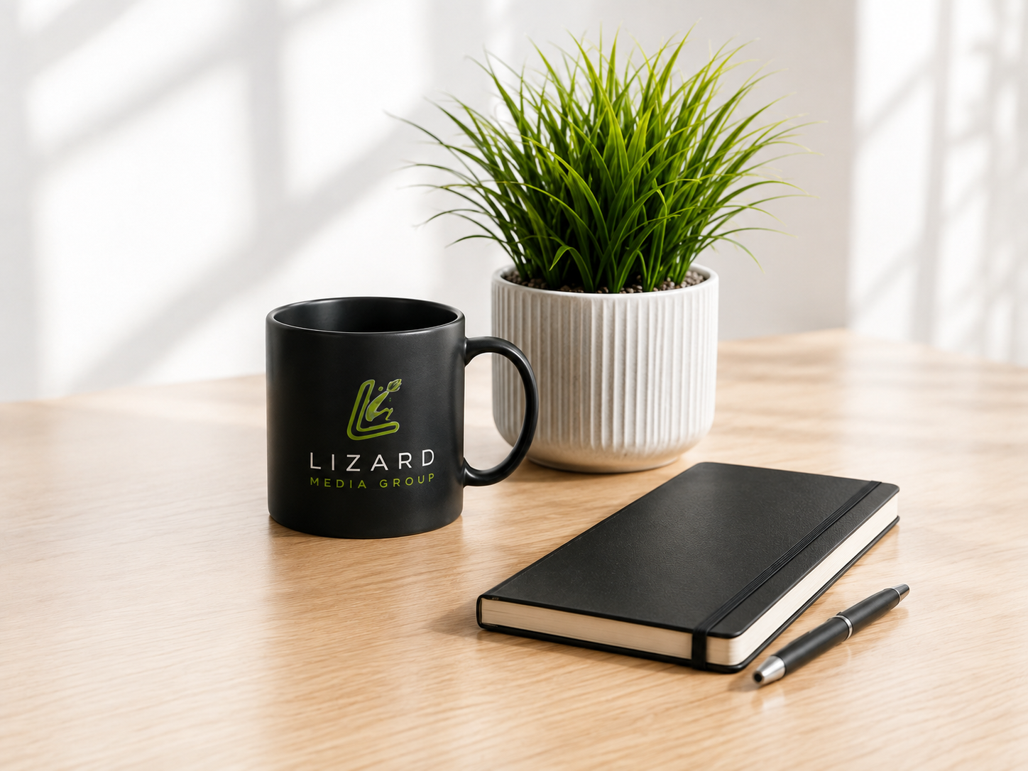 Lizard Media branded mug beside a plant, notebook and pen on a light wood desk